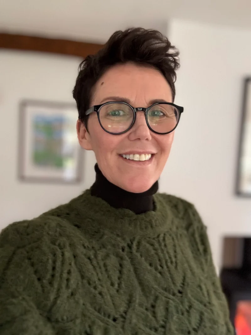 A photo of Cal, qualified counsellor and psychotherapist in Carnforth. Cal is wearubg a greeb hynoer and smiling.